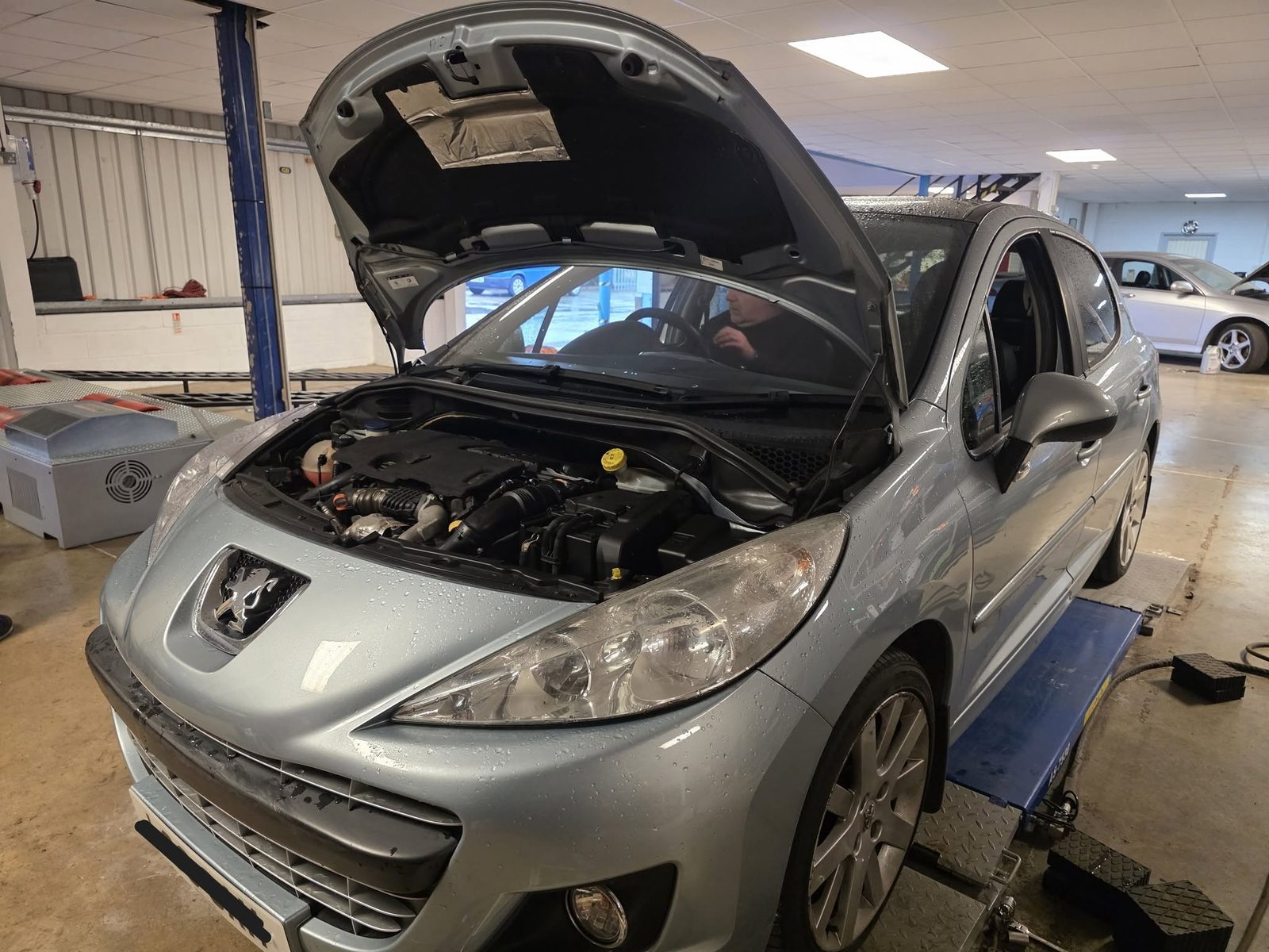 Silver Peugeot 207 with the bonnet up in the Ace Auto Works workshop