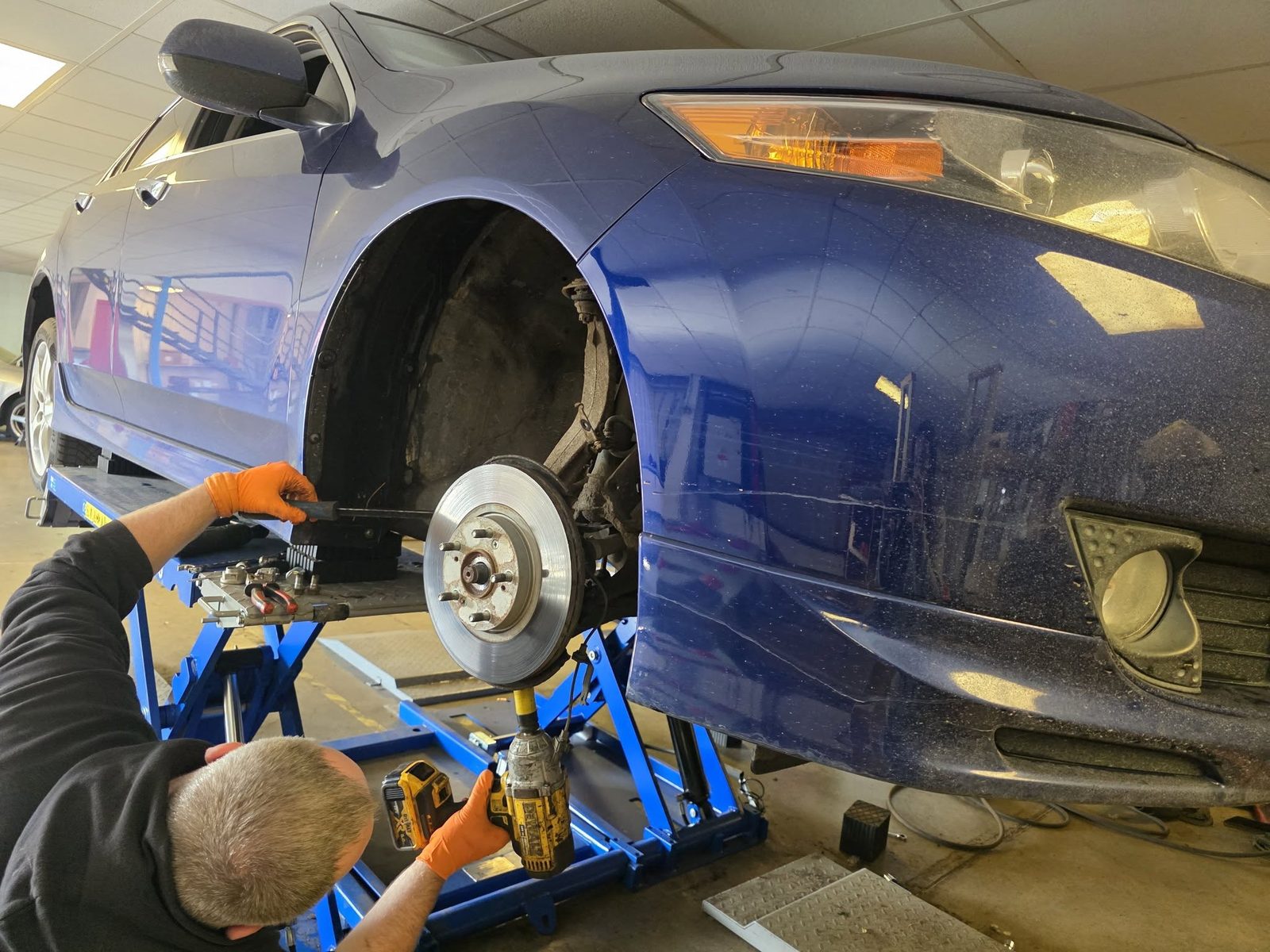 Mechanic using an impact gun on a front wheel hub of a blue Honda