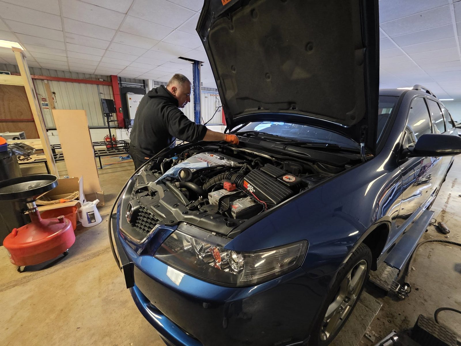 Mechanic leaning into the engine bay of a blue Honda