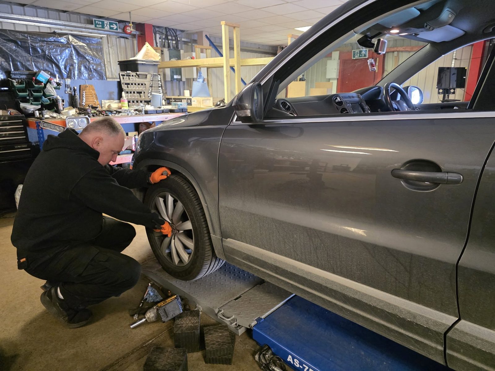 Mechanic crouched at the front wheel of a grey Volkswagen Tiguan