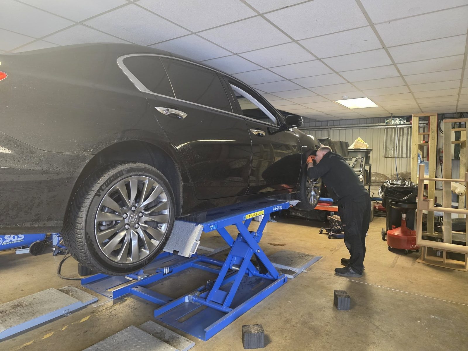 Black Honda raised on a scissor lift with a mechanic underneath