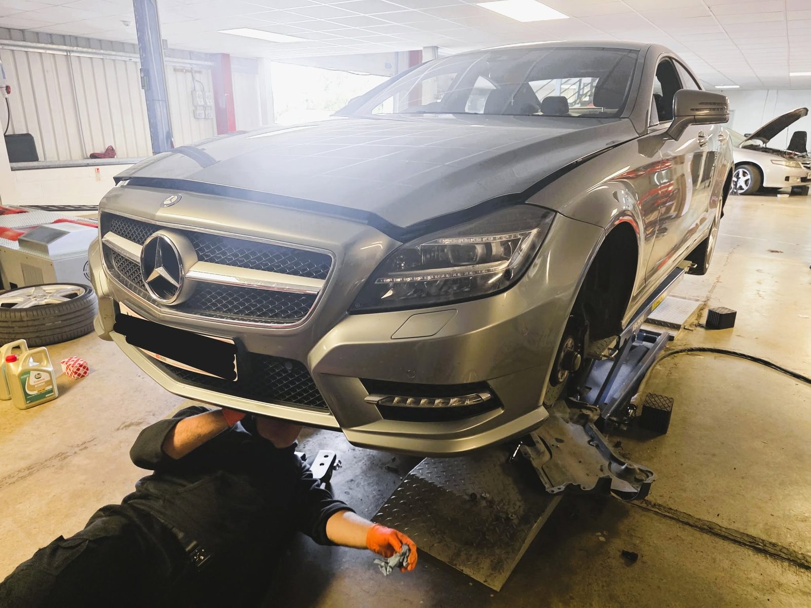 Mechanic lying under the front of a silver Mercedes
