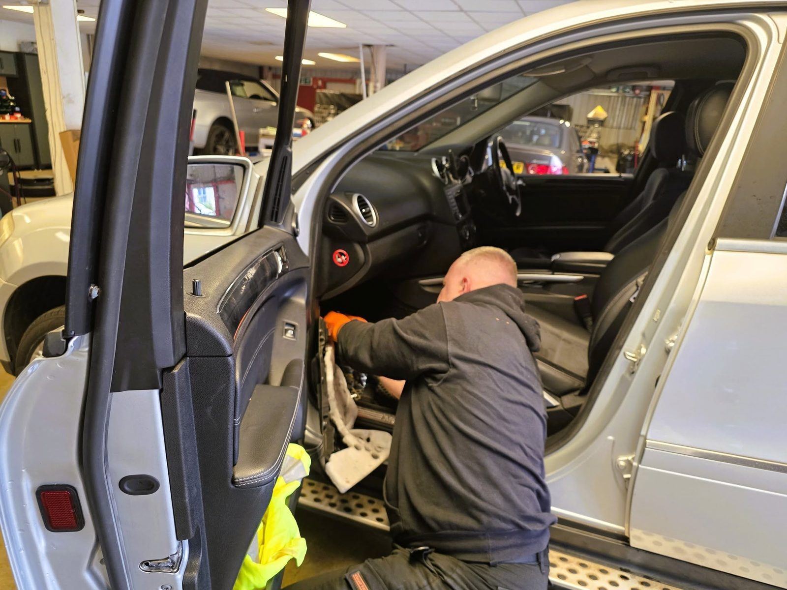 Mechanic working inside the door and footwell of a silver Mercedes