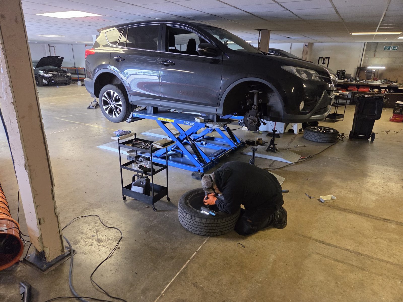Mechanic working on a tyre beside a RAV4 on a scissor lift