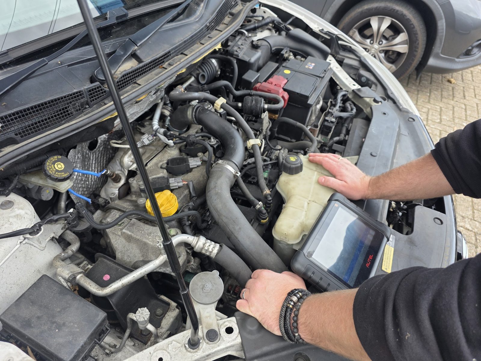 Diagnostic tablet resting in an engine bay while a mechanic works