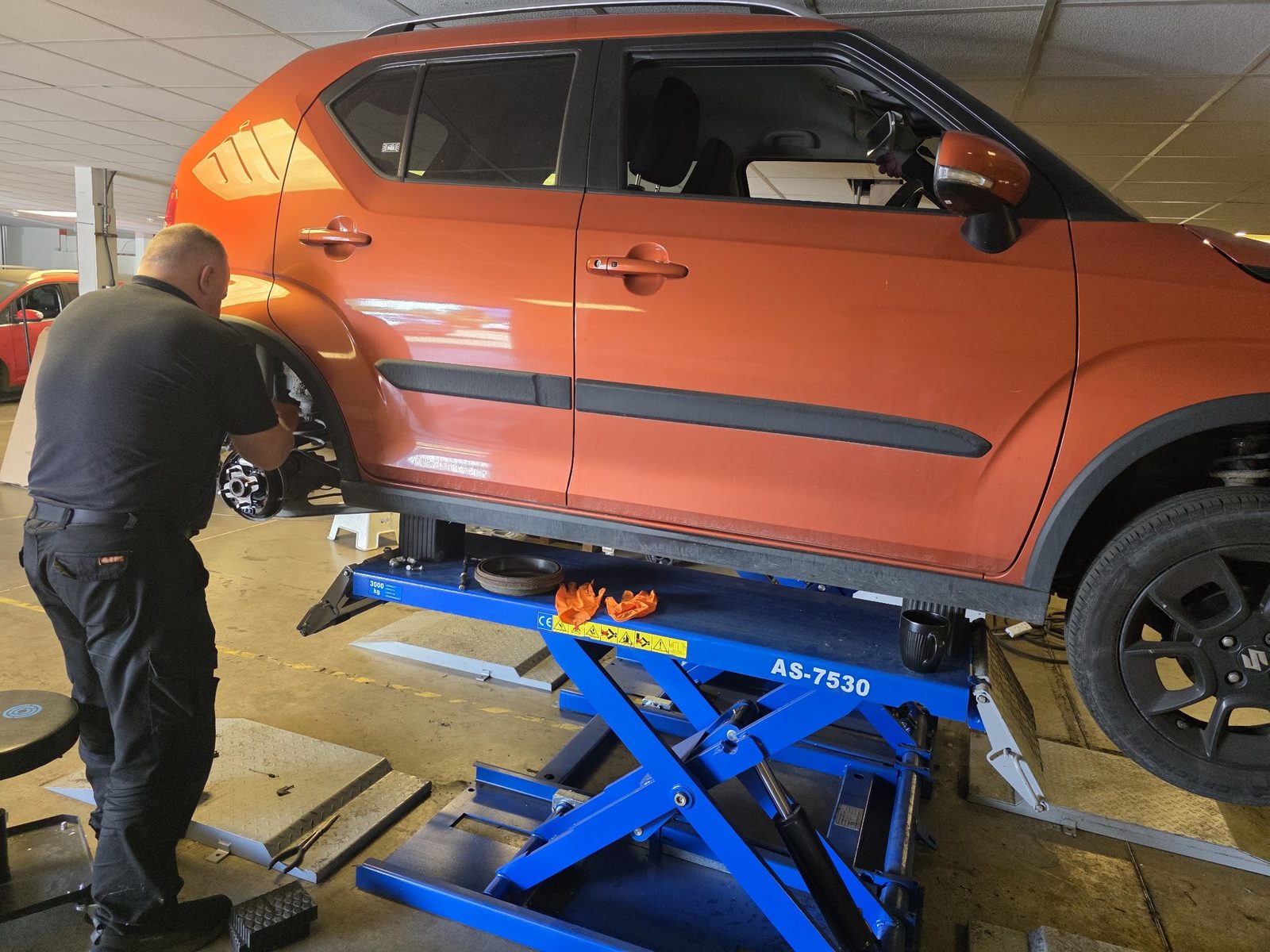 Mechanic working at the wheel of an orange Suzuki on a blue scissor lift