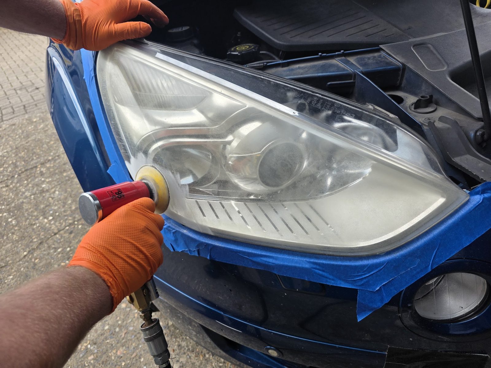 A headlight being polished with the surrounding paint masked off